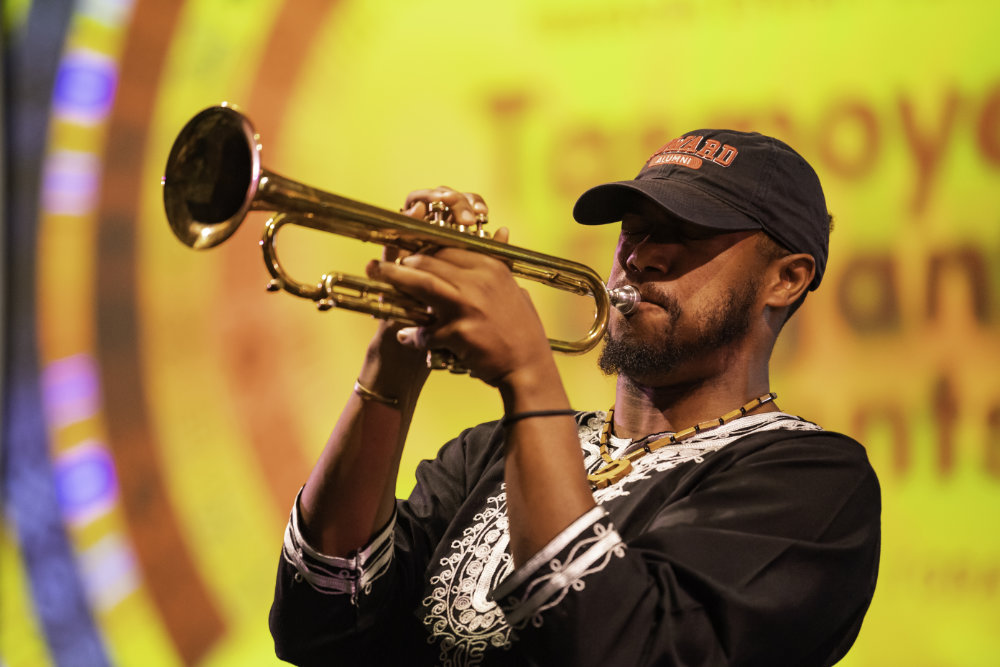 Black man plays the trumpet in front of a brightly colored screen.