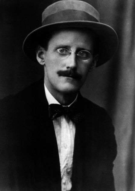 Black and white image of James Joyce circa 1917 in a hat, eyeglasses, bow tie, pince-nez, and suit.