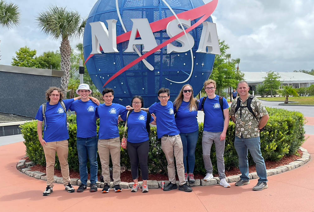 Group of Rochester students and their faculty advisor in front of NASA sign.