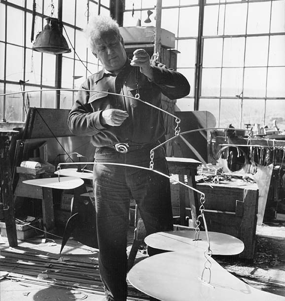 Alexander Calder manipulating mobile in his art studio.