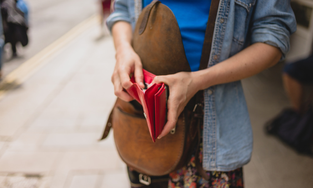 Woman opening her purse and holding a red wallet.