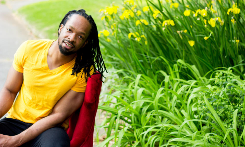Feature image Jericho Brown seated in a red chair in a field of flowers.