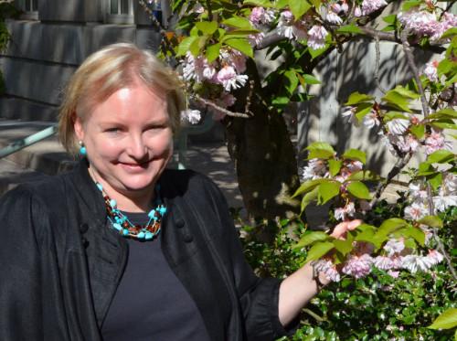 Cindy Gary smiles next to a flowering shrub.