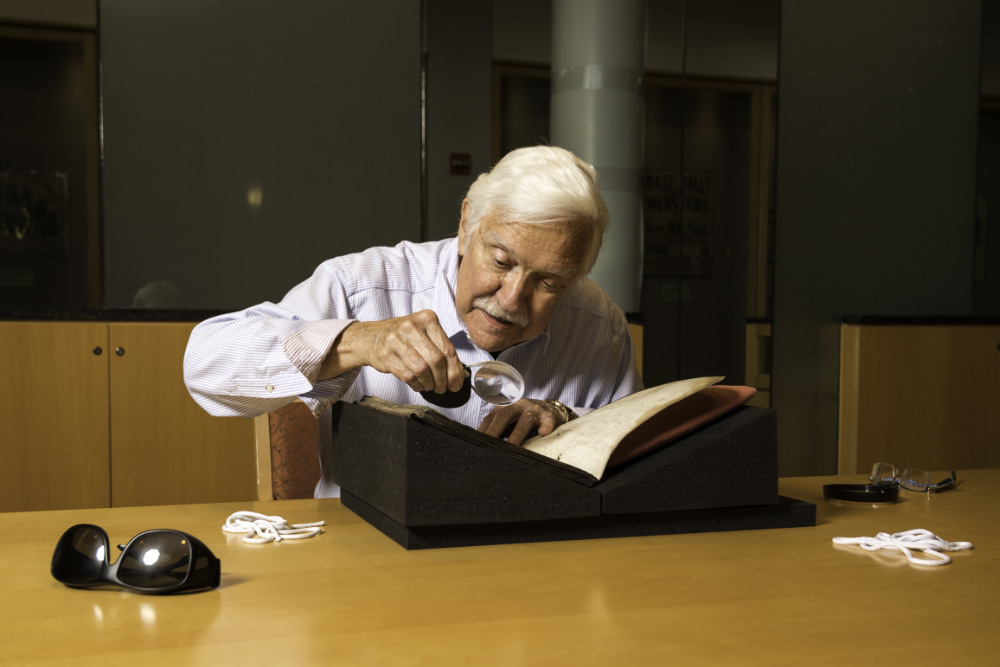 Richard Kaeuper holds a magnifying glass while inspecting the first medieval manuscript in the new Kaeuper Collection.