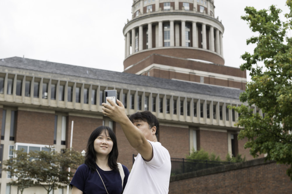Father and daughter take a selfie with Rush Rhees Library in the background. 