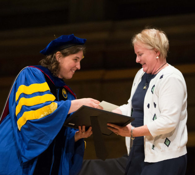 Wendi Heinzelman in commencement regalia hands an award to Cindy Gary.