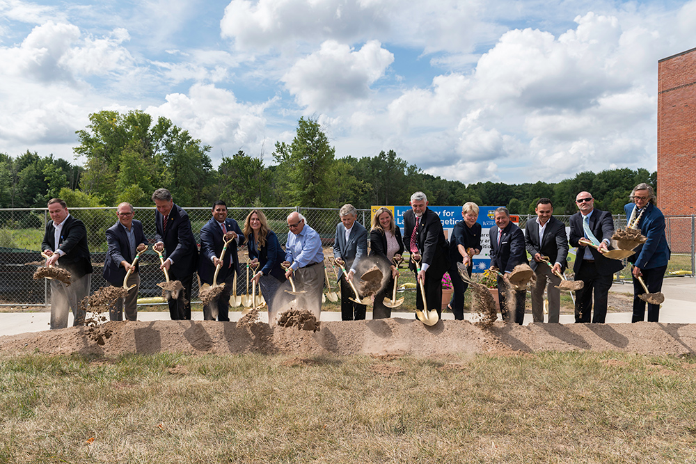 group photo of more than a dozen people each holding a shovel and lifting a shovelful of dirt.