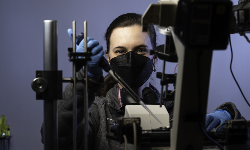 young woman wearing a black face mask in front of a microscope..