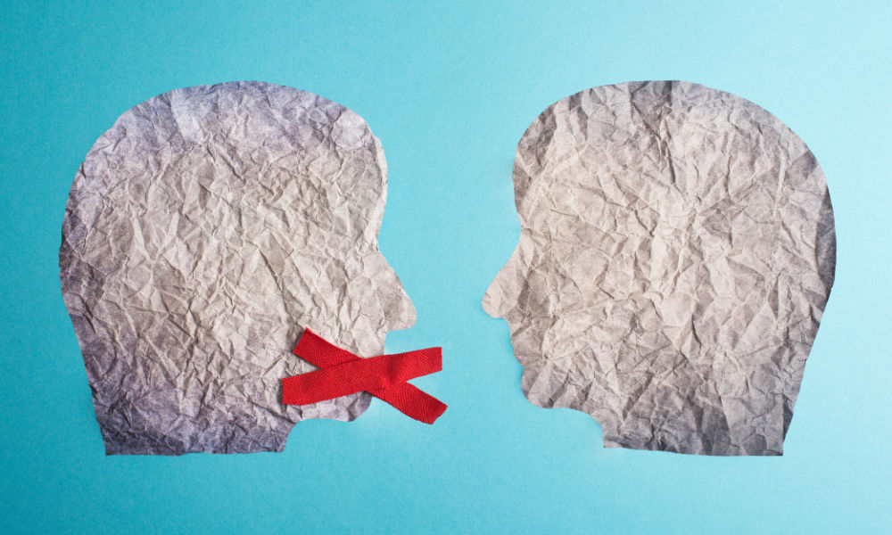 Two silhouetted faces cut from crumpled paper face one another, one with red tape over its mouth.