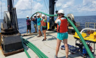 researchers stand in a line on a boat holding a large hose.