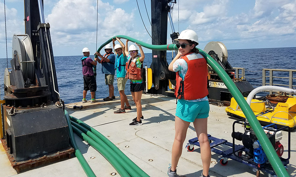 researchers stand in a line on a boat holding a large hose.