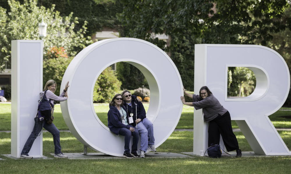 Four women pose for photos on the IOR letters on the Eastman Quad.