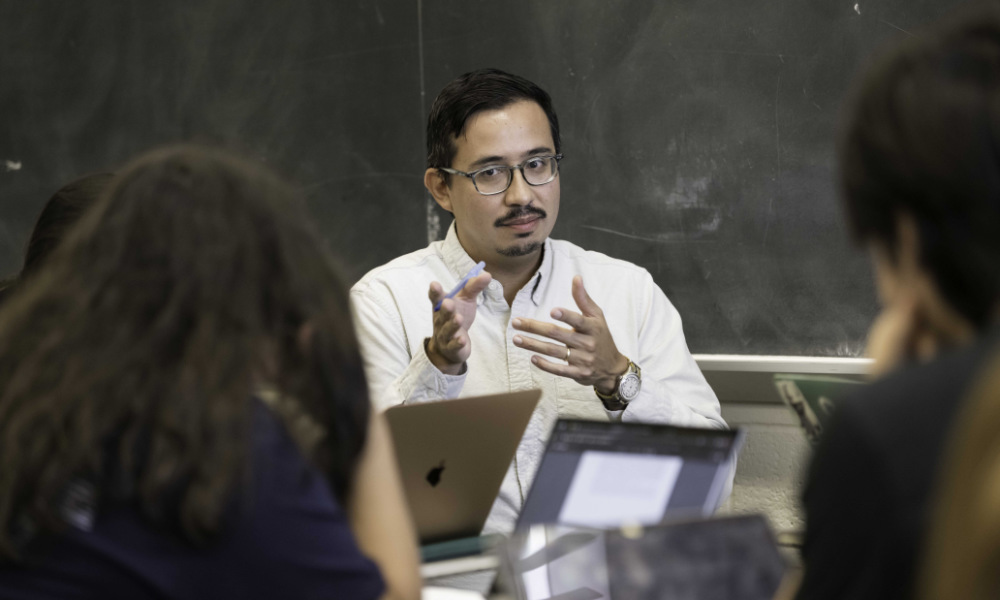 Pablo Sierra Silva sits and gestures while teaching among a couple of students seen from behind.