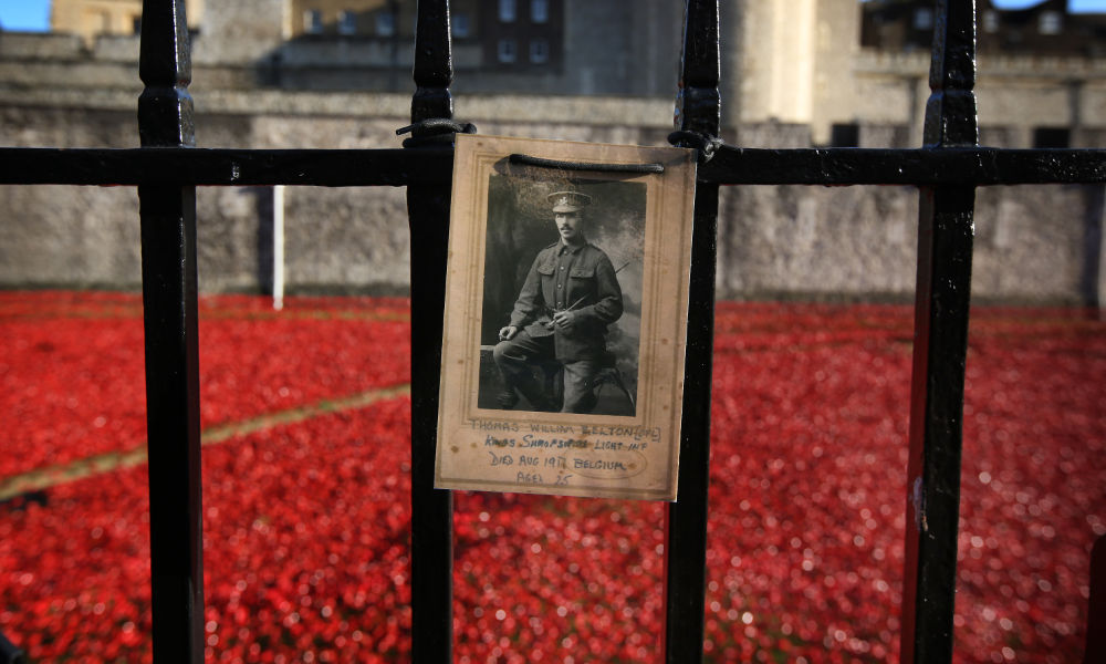 Black-and-white photo of a solider pinned to a gate in front of a sea of ceramic poppies to symbolize World War I memorialization.