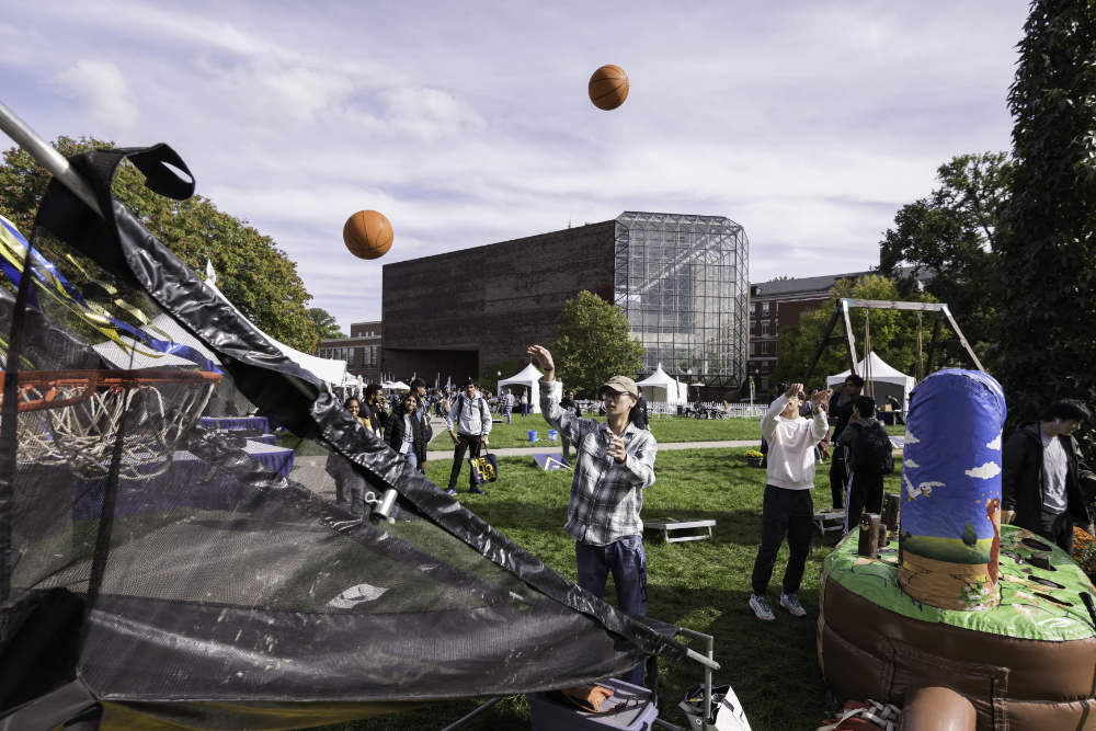 People shooting hoops and milling about with tents and Wilson Commons in the background on the Wilson Quadrangle.
