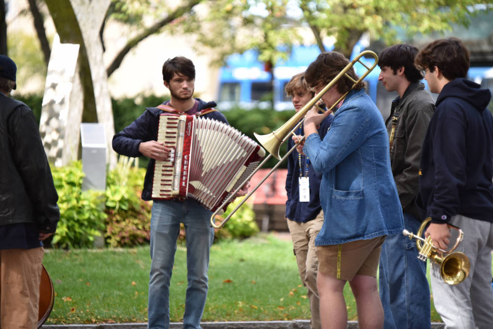 Eastman School of Music performers with an accordion, trombone, and other instruments play outside. 