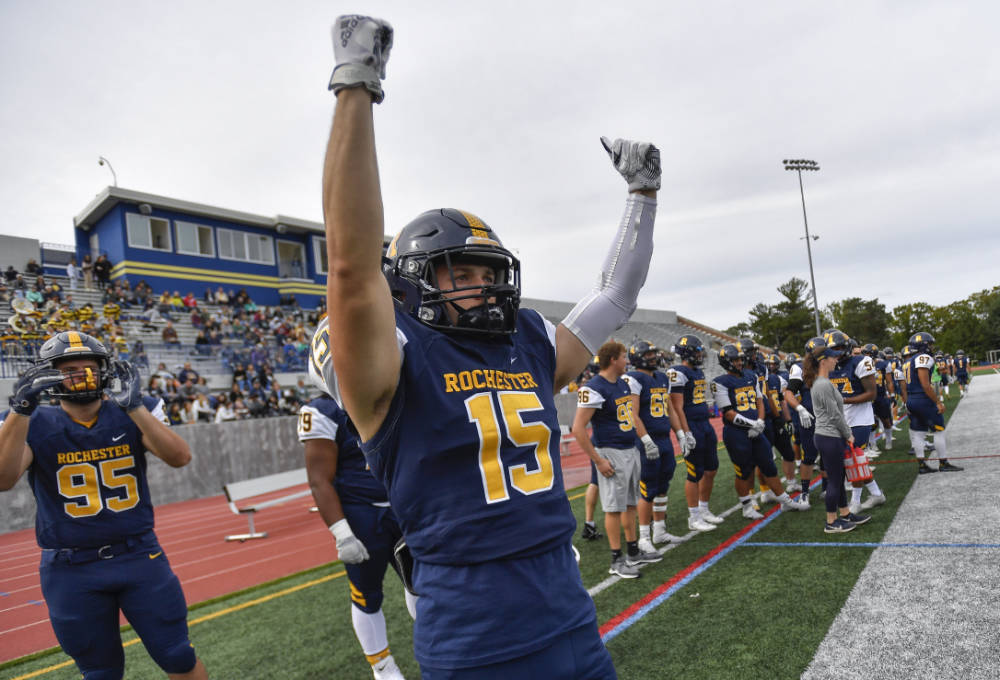 Football player with arms raised while fellow players and supports cheer in the background.