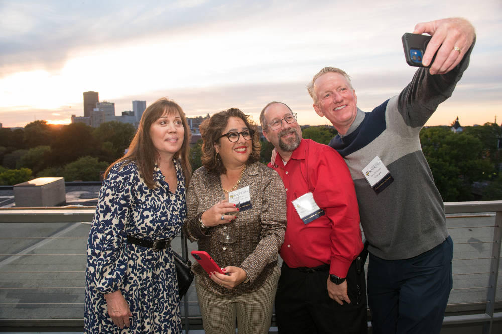 Four people taking a selfie at sunset with the city of Rochester skyline in the background.