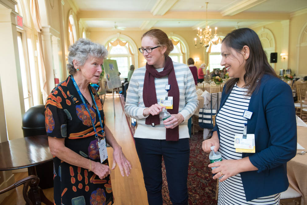 Three people wearing badges and having a conversation in a sunlit room.