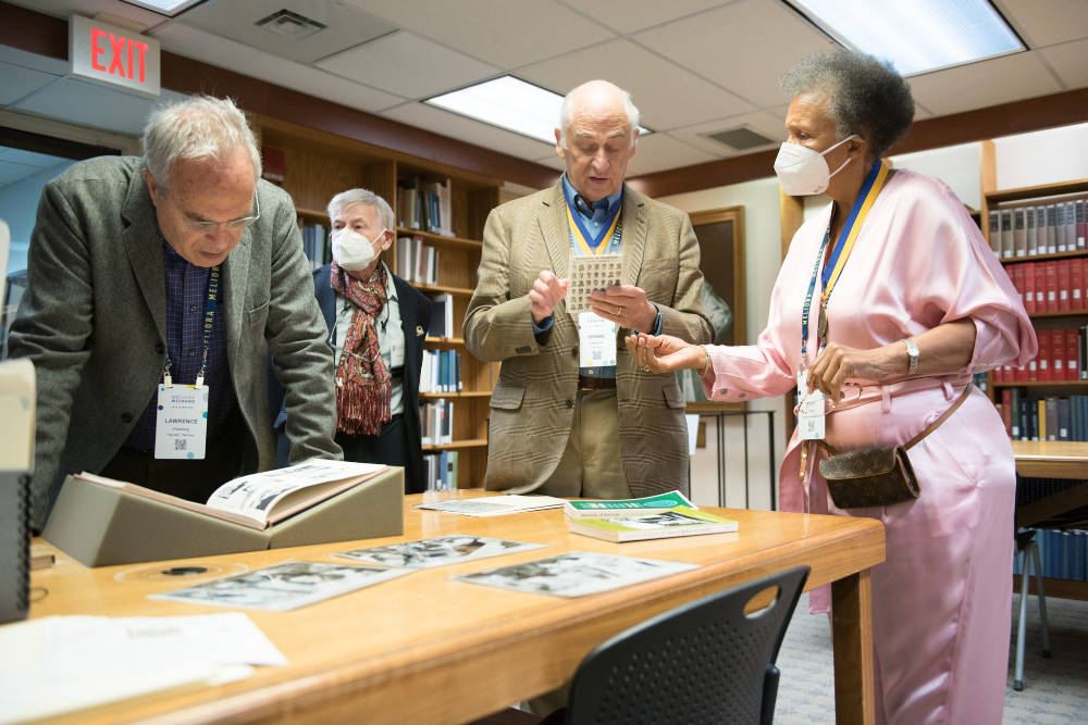 Four elderly people gather around a table to look at library memorabilia on display.