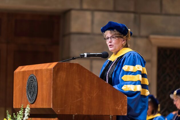 Kathy Rideout speaking at podium in hat and gown at School of Nursing commencement.