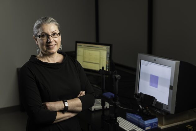 Krystel Huxlin smiling, arms folded, in lab next to computer screens.