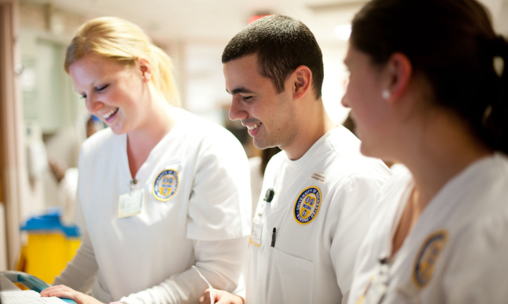 A trio of University of Rochester School of Nursing students in uniform examine a patient's chart.