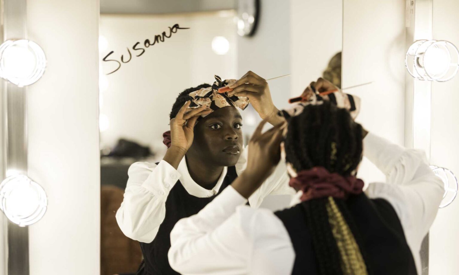 Actor playing Susanna in The Crucible fixes her costume in a mirror backstage.