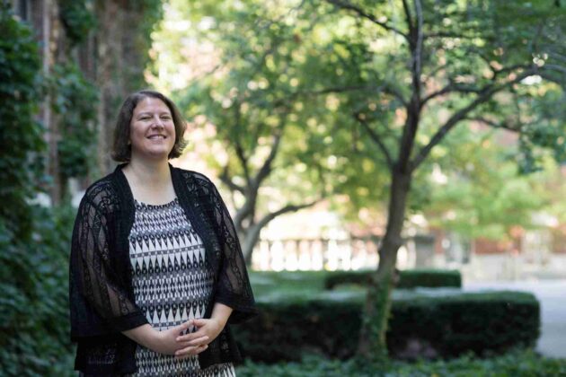 Rachel Remmel stands with her hands folded in front of her for a photo on the Eastman Quad. 