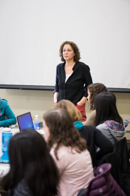 Deborah Rossen-Knill stands in front of a Writing, Speaking, and Argument class with students seated nearby.