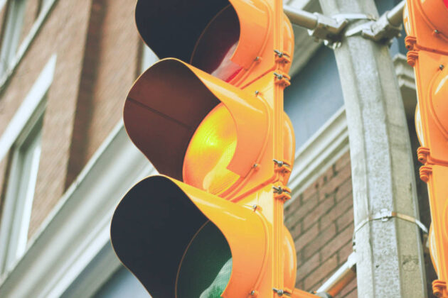 Close-up of a traffic signal with the yellow light lit up in a city. 