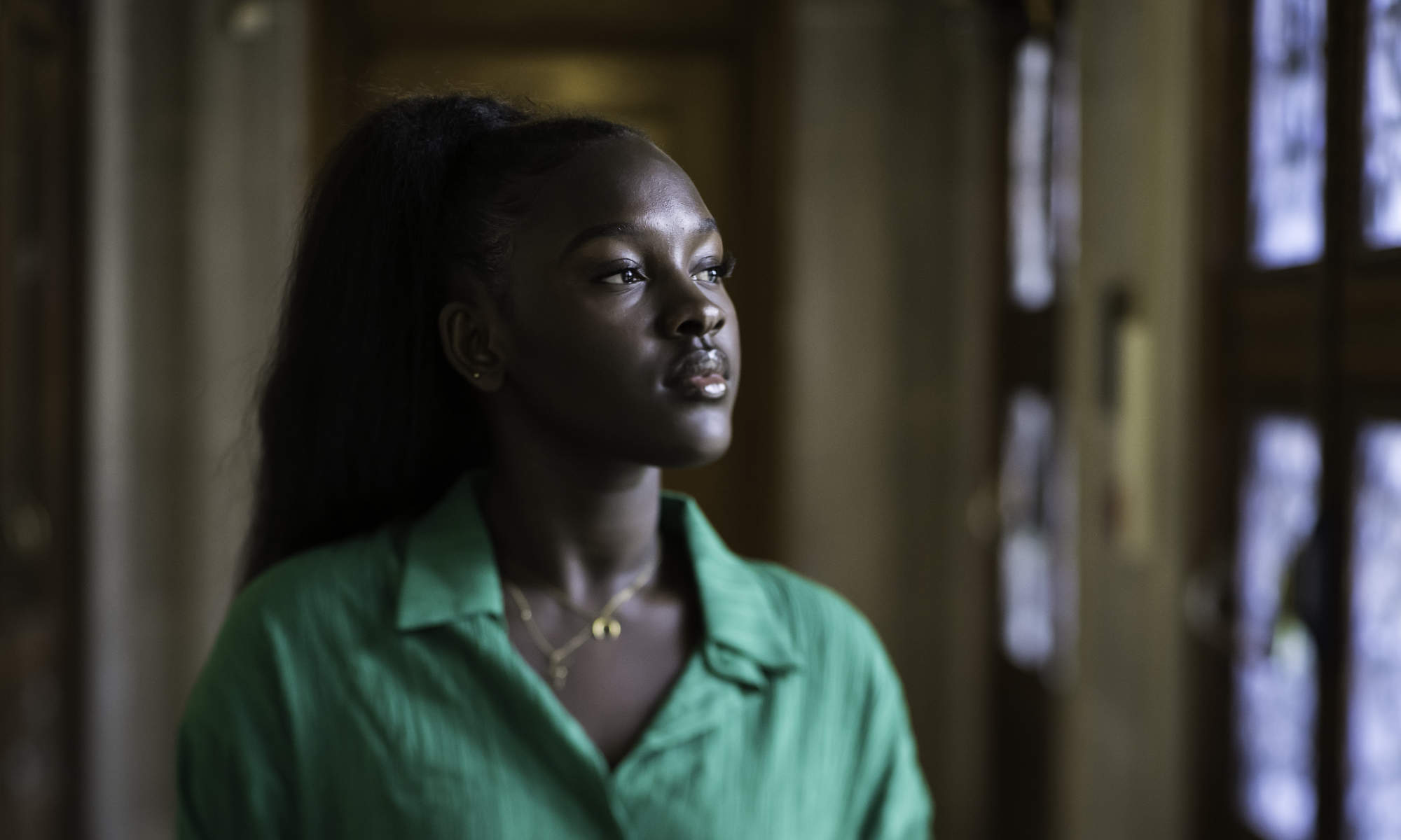 Fatou Jobe, who is translating Wolof fables into English, wears bright green while looking off camera in a library entryway.