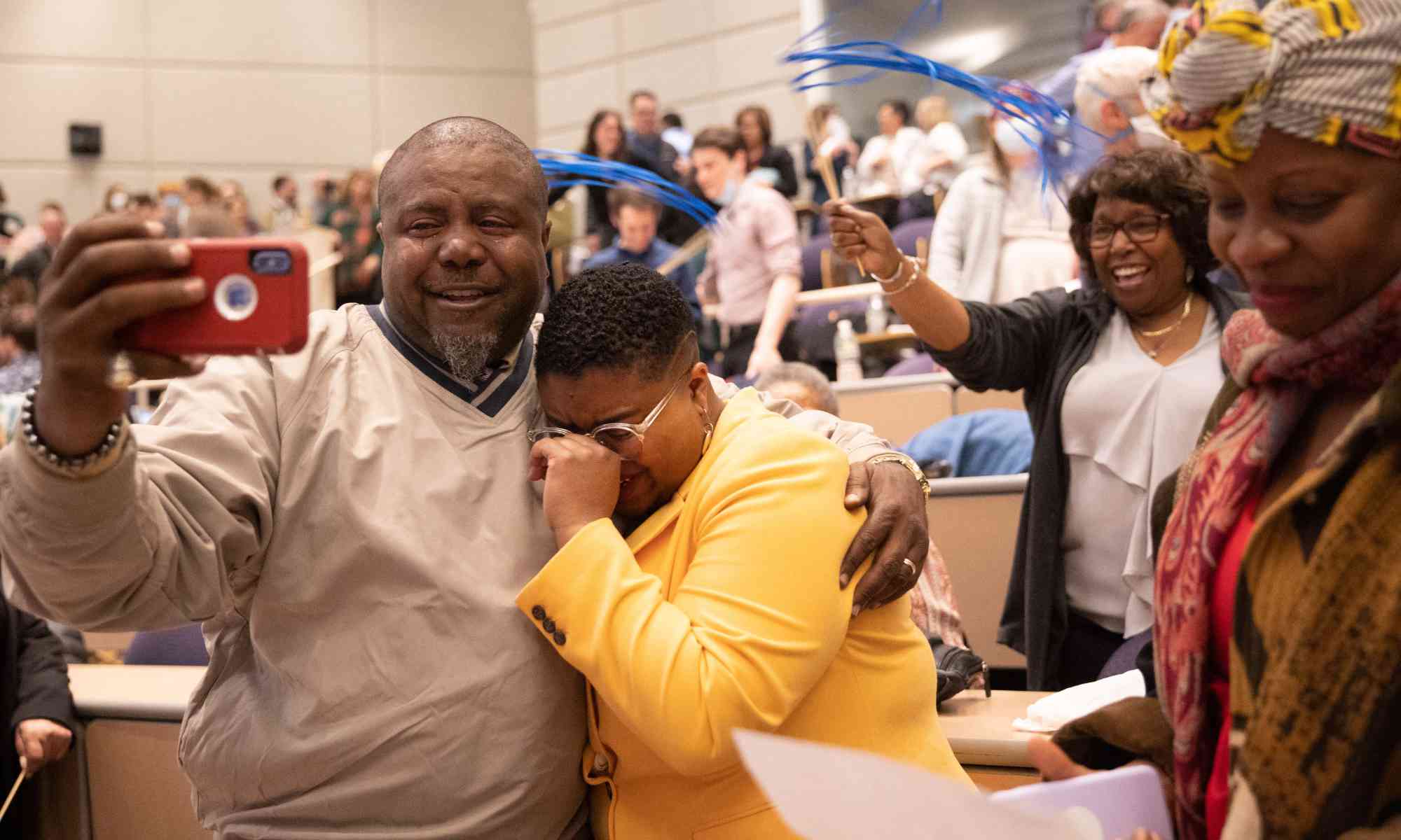 Father holds a phone and embraces his child, who has just learned her Match Day 2023 placement.