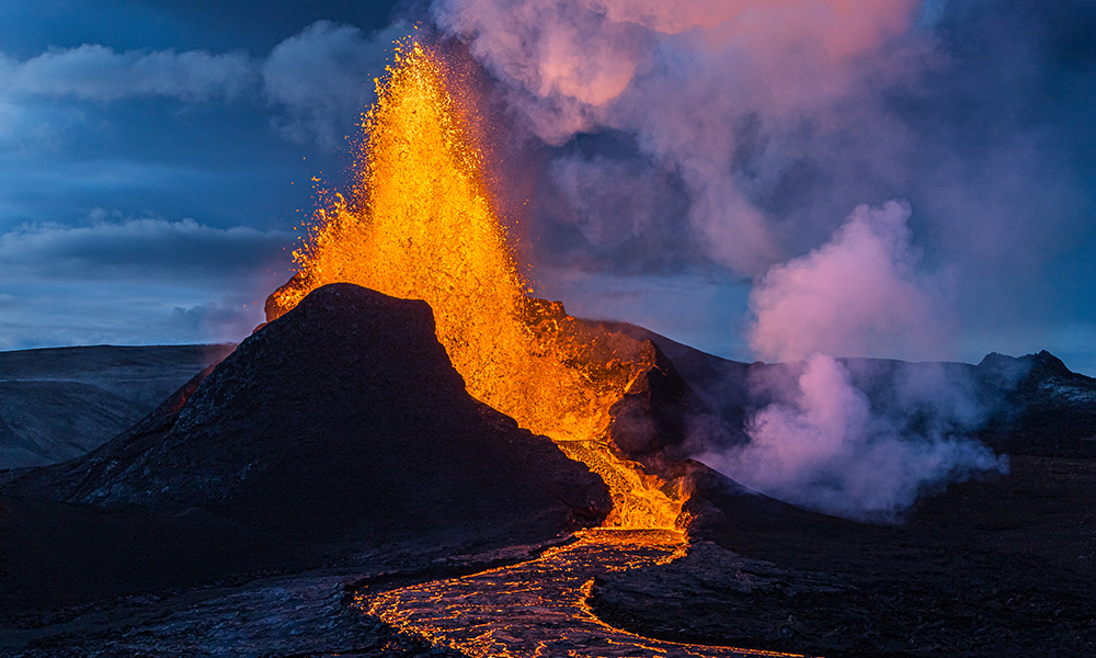 Feature image Volcano erupting, shooting bright red lava high into a purple cloudy sky.