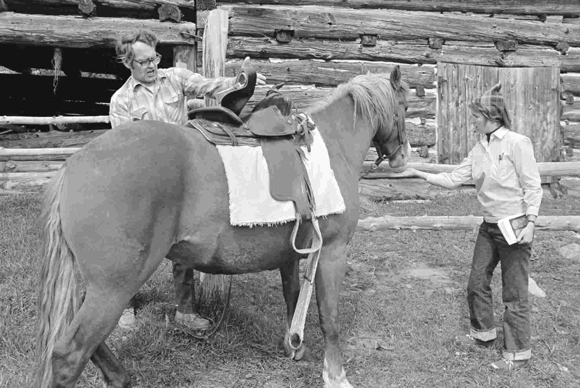Black and white archival photo of Russell Peck saddling a horse with a student nearby.