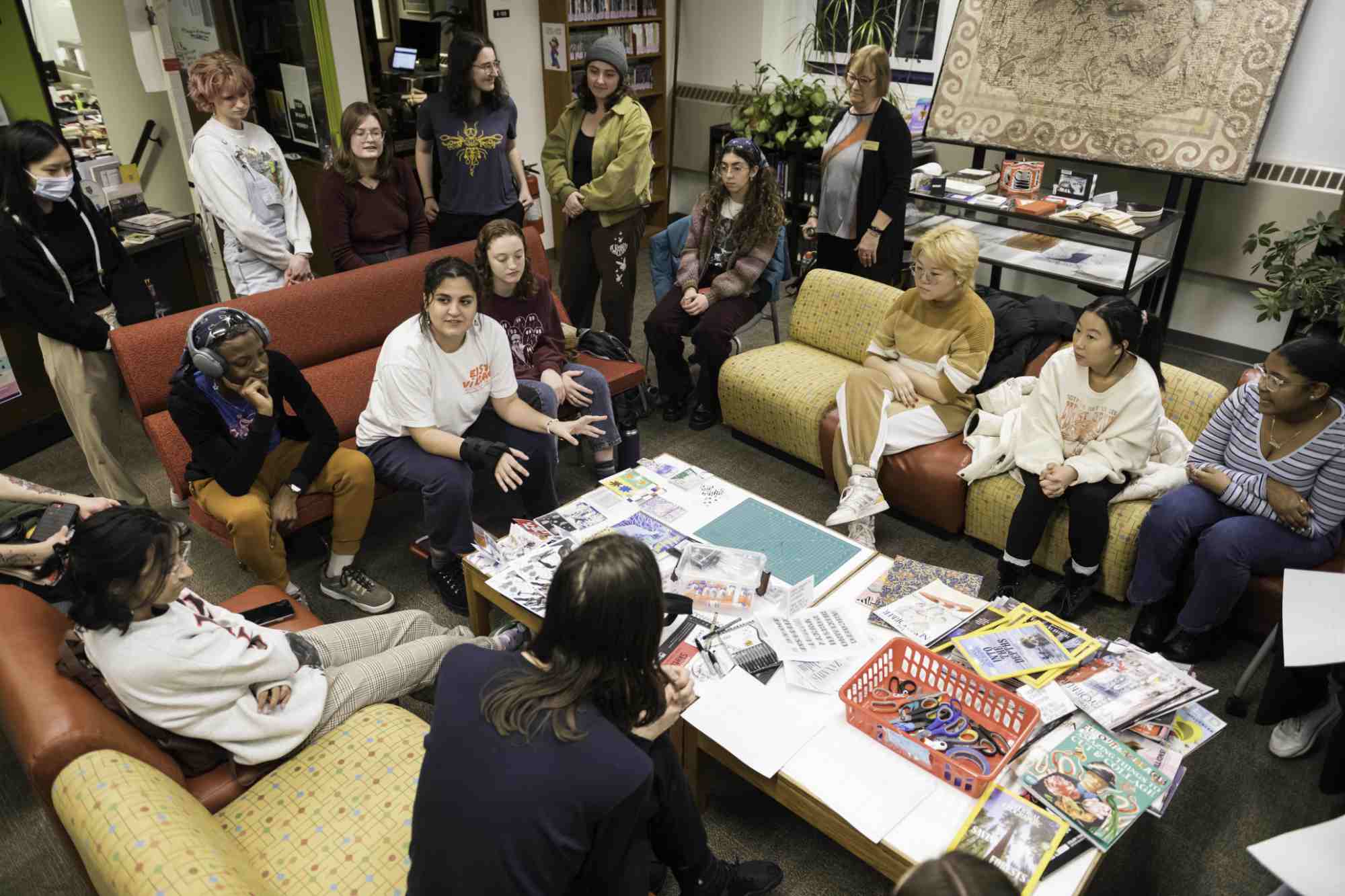 Angelica Aranda surrounded by students and art supplies leading a zine-making workshop on campus.