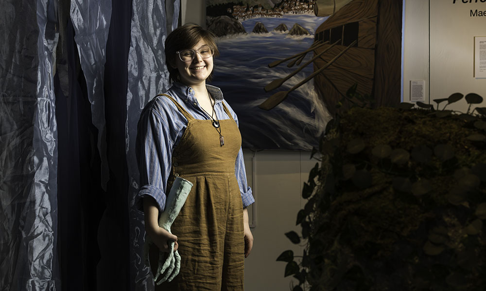 Mae Cooke, from head to knee, smiling in center with painting and sculpture in background.