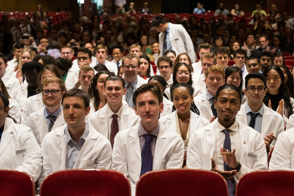 An auditorium of students wearing white doctor's coats. 