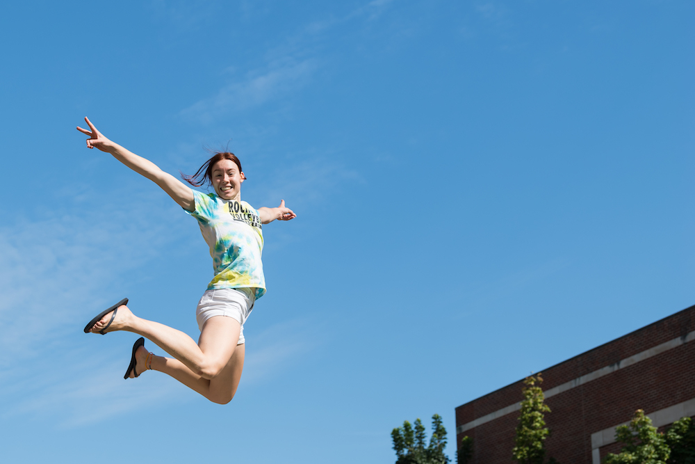 Student jumping high with blue sky behind them. 