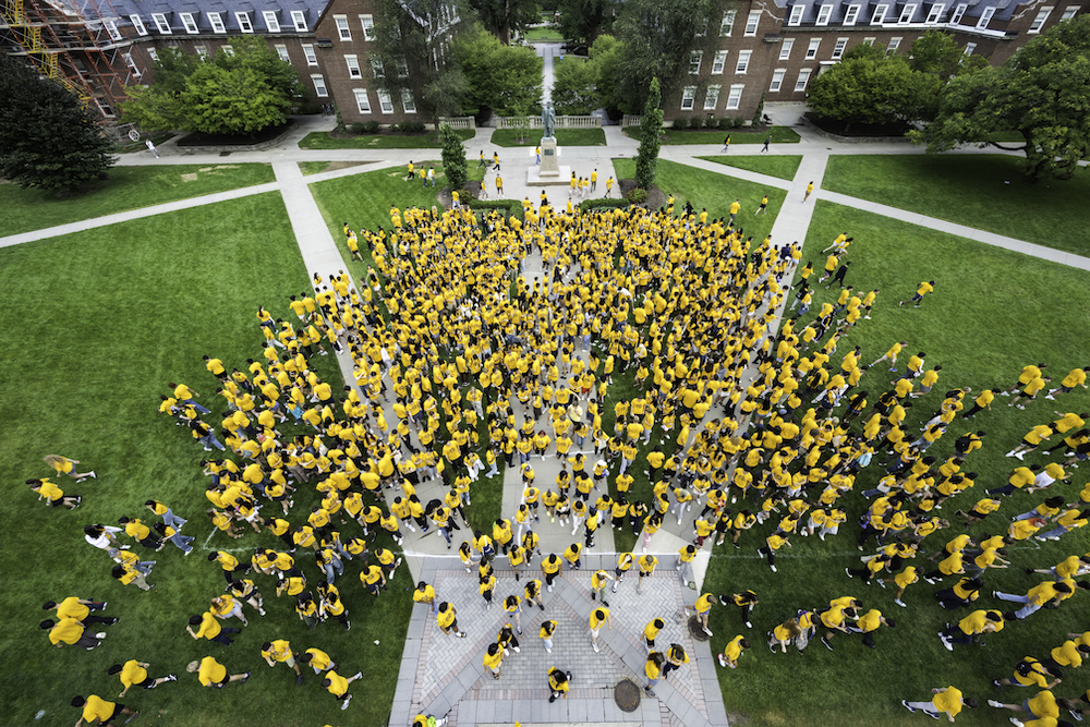 Aerial photo of students in yellow T-shirts on a green grass quad dispersing. 