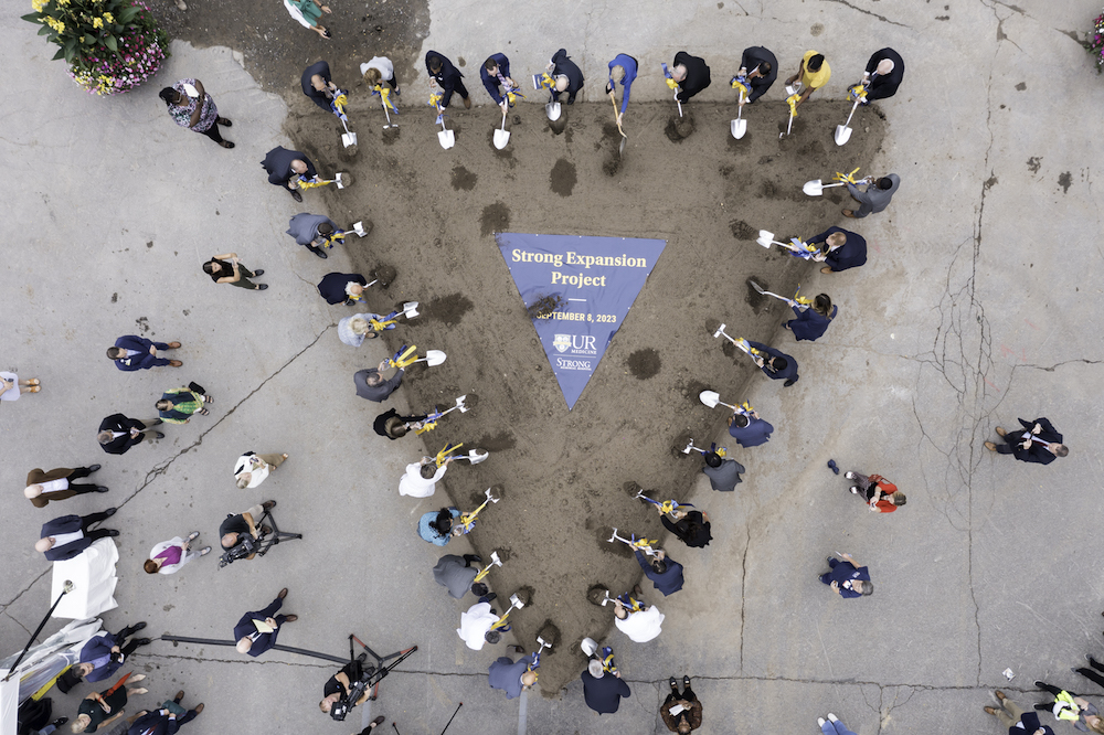 From above, a triangle is formed with people holding shovels on all sides. The words "Strong Expansion Project" are in the middle of the dirt.