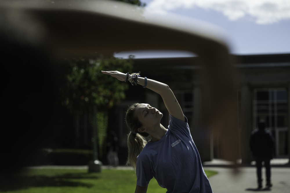 Student in blue T-shirt with an arm over their head, in a yoga pose