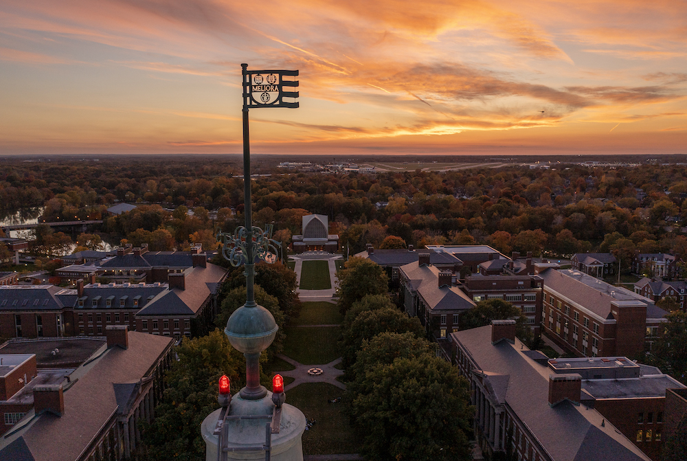 Aerial drone photo of Meliora weathervane atop Rush Rhees Library Tower, as seen during sunset
