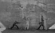 Black-and-white photo of a street art mural depicting a tug-of-war between a Russian and Ukrainian soldier.