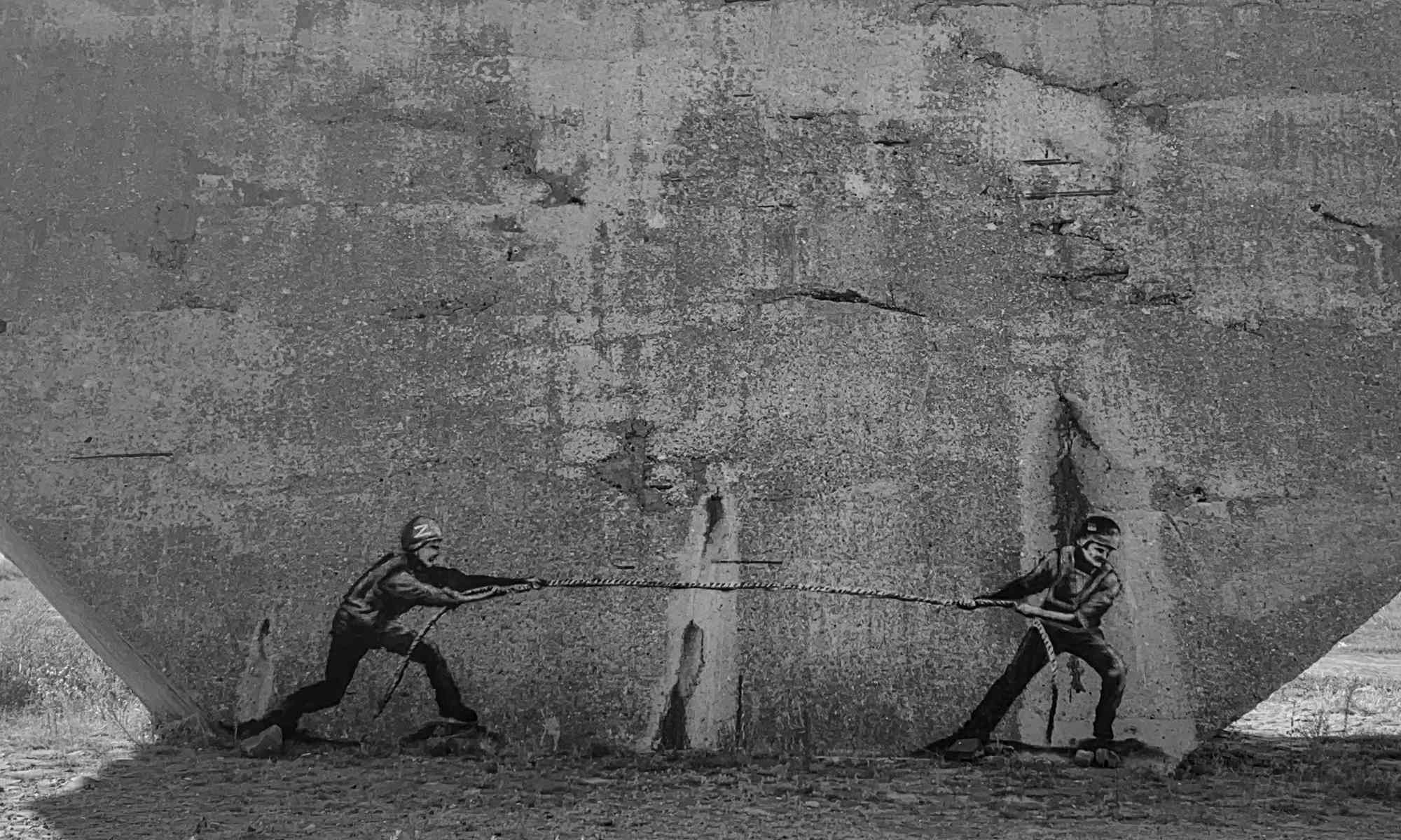 Black-and-white photo of a street art mural depicting a tug-of-war between a Russian and Ukrainian soldier.