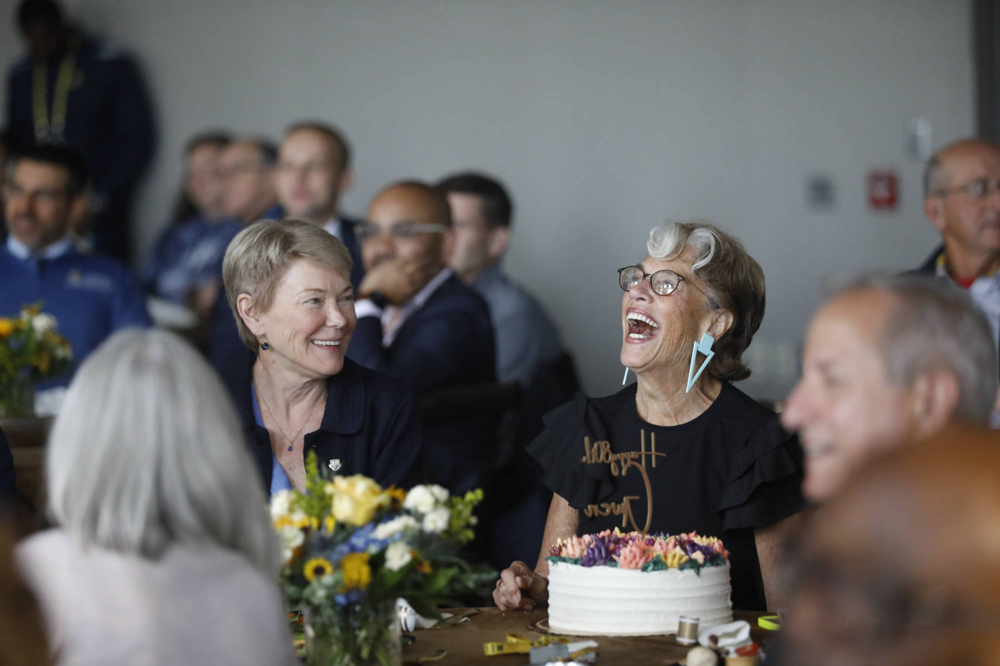 Gwen Greene surrounded by people and smiling with a birthday cake on the table in front of her.