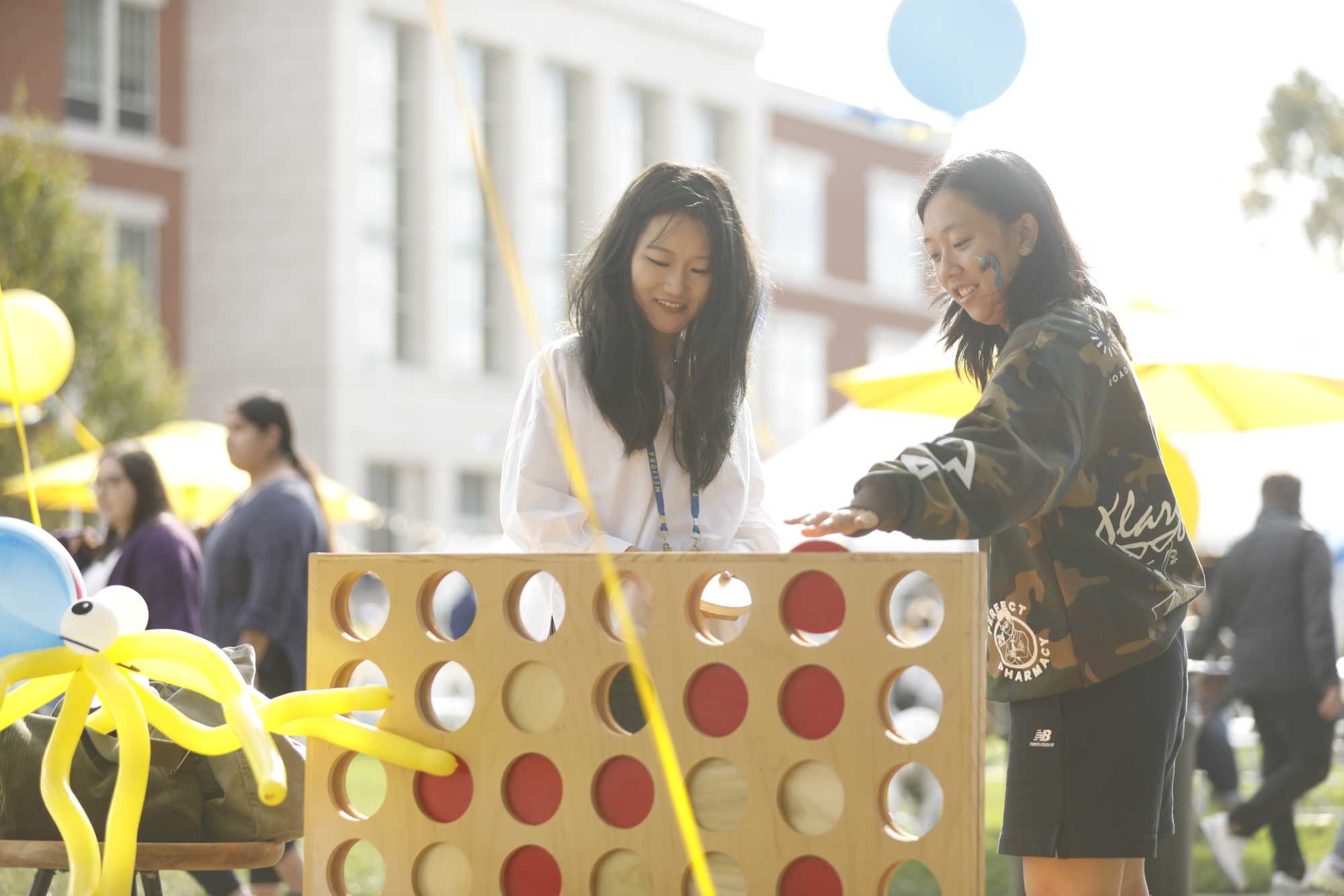 Two women playing a giant Connect Four game in the Meliora Village.