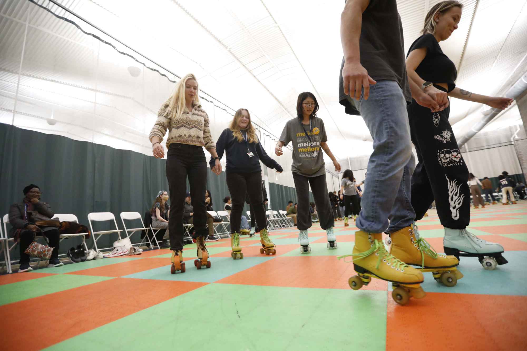 University of Rochester students and community members roller skating on a green-and-orange checkered floor.