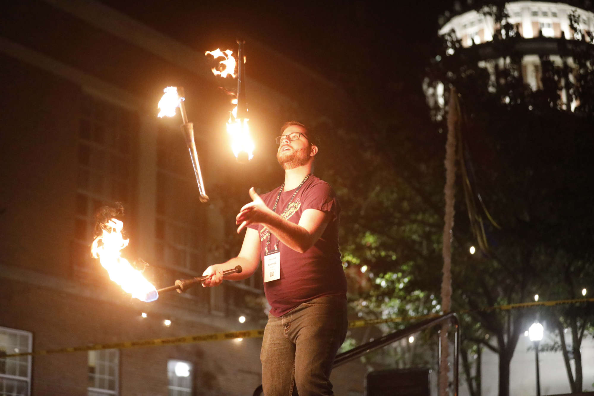 Man juggling several items that are on fire while it is dark outside.