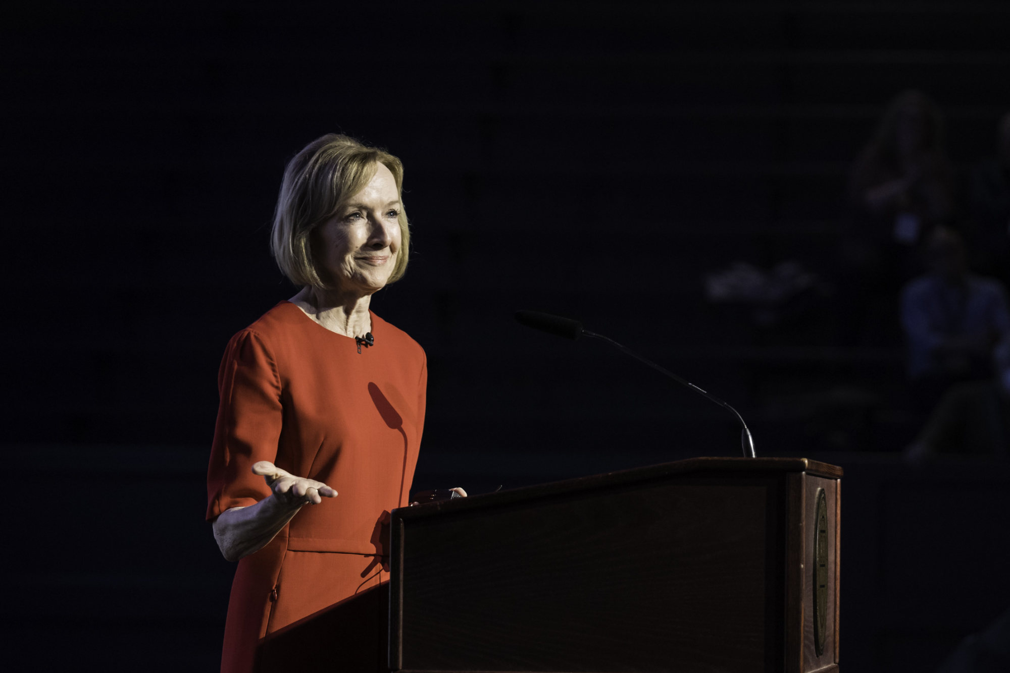 Meliora Weekend 2023 keynote speaker Judy Woodruff in a red dress at a podium against a black background.